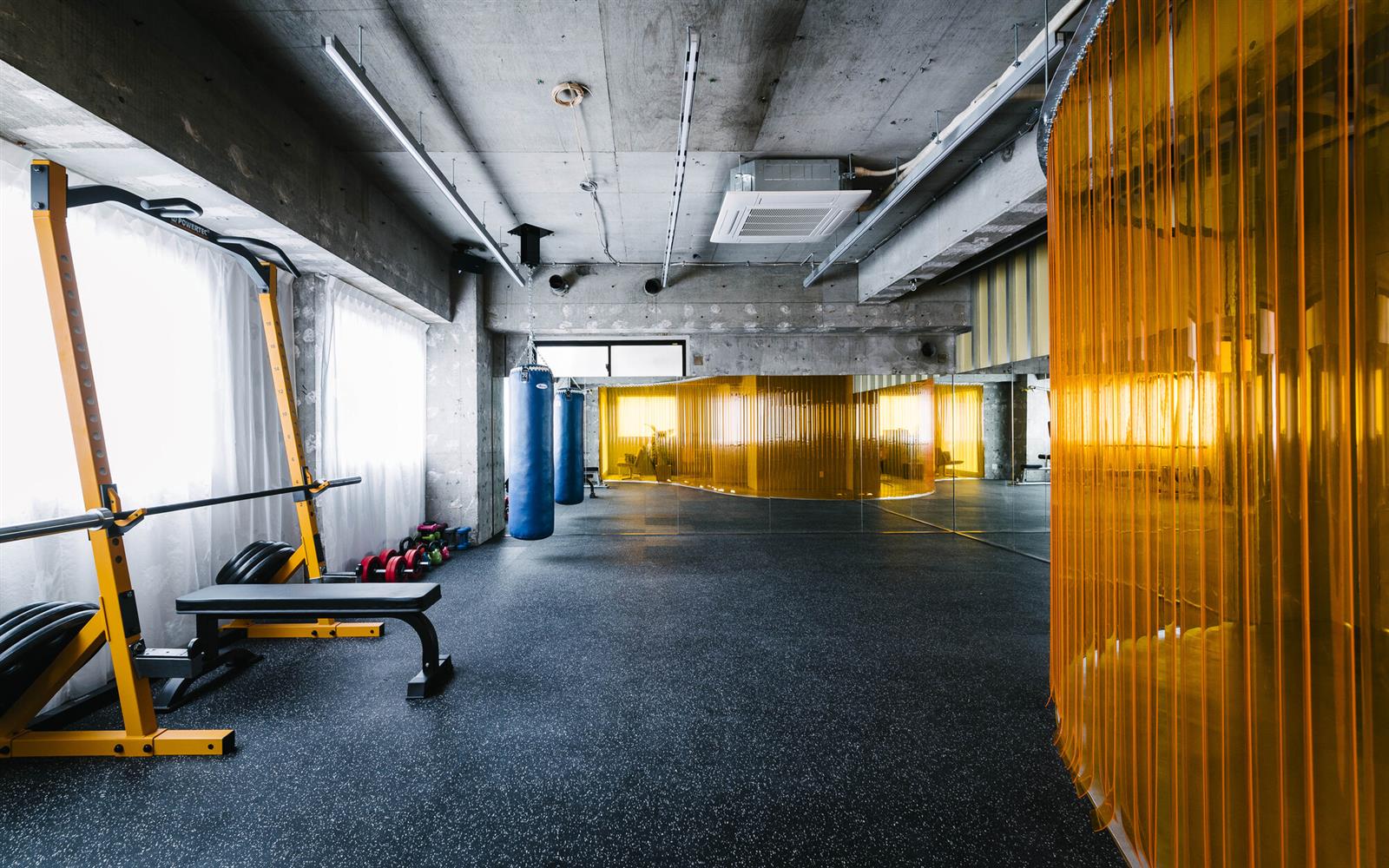 طراحی باشگاه بدنسازی کوچک: سالن تمرین CELL Gym ژاپن با پرده منحنی نارنجی، رک و نیمکت کنار پنجره