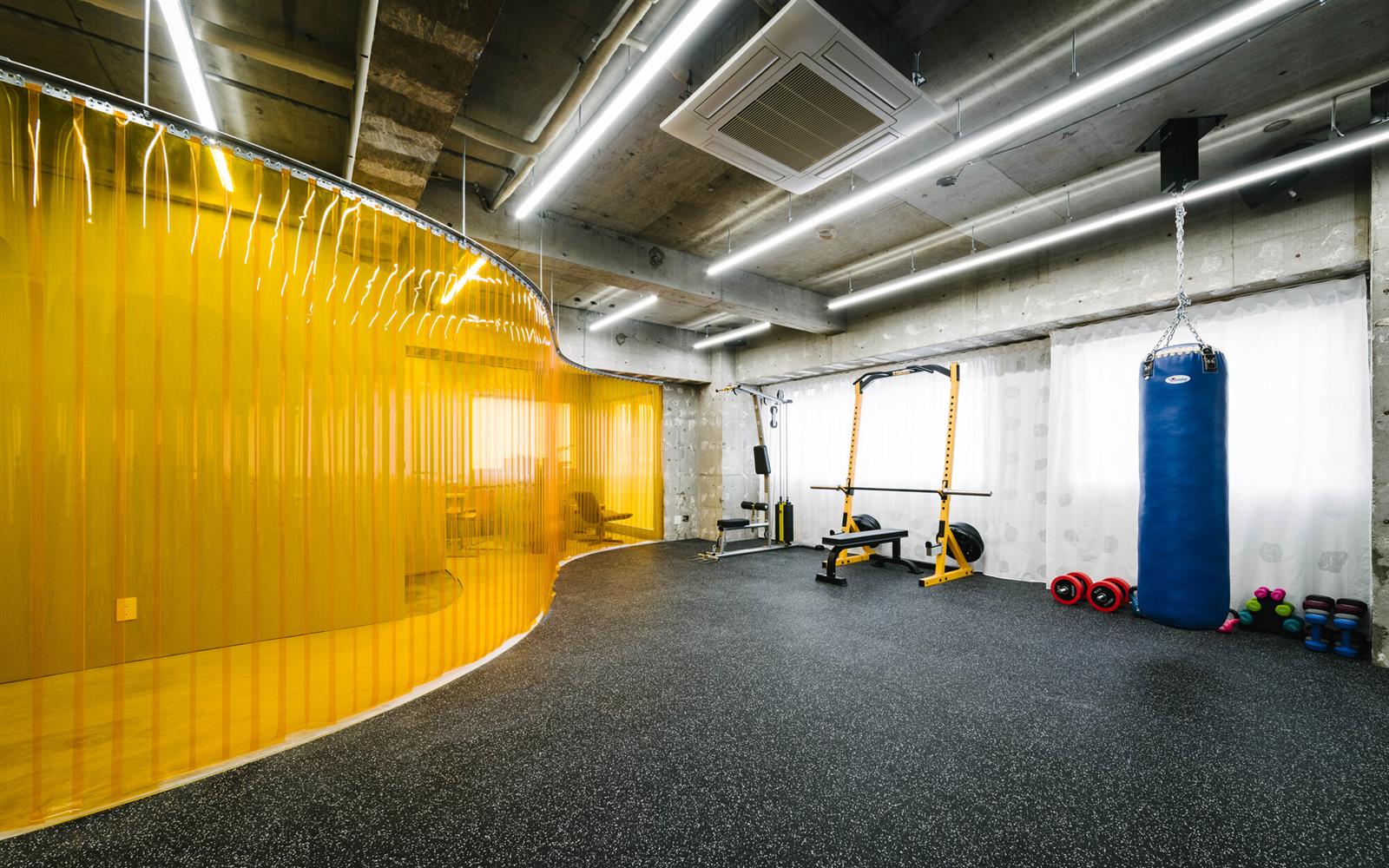 کف لاستیکی تیره، سقف بتنی نمایان و چراغ خطی در سالن CELL Gym، نمونه طراحی باشگاه مدرن با سقف نمایان