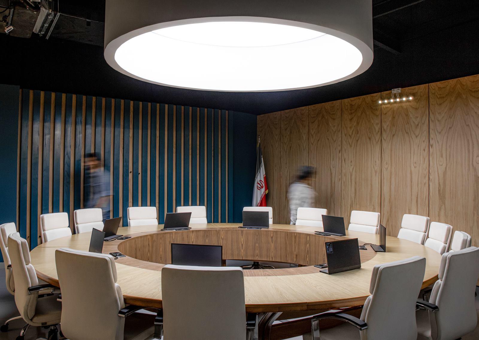 پنل نورانی گرد بزرگ با نور یکدست روی میز جلسات و چند نور تاکیدی روی دیوار چوبی